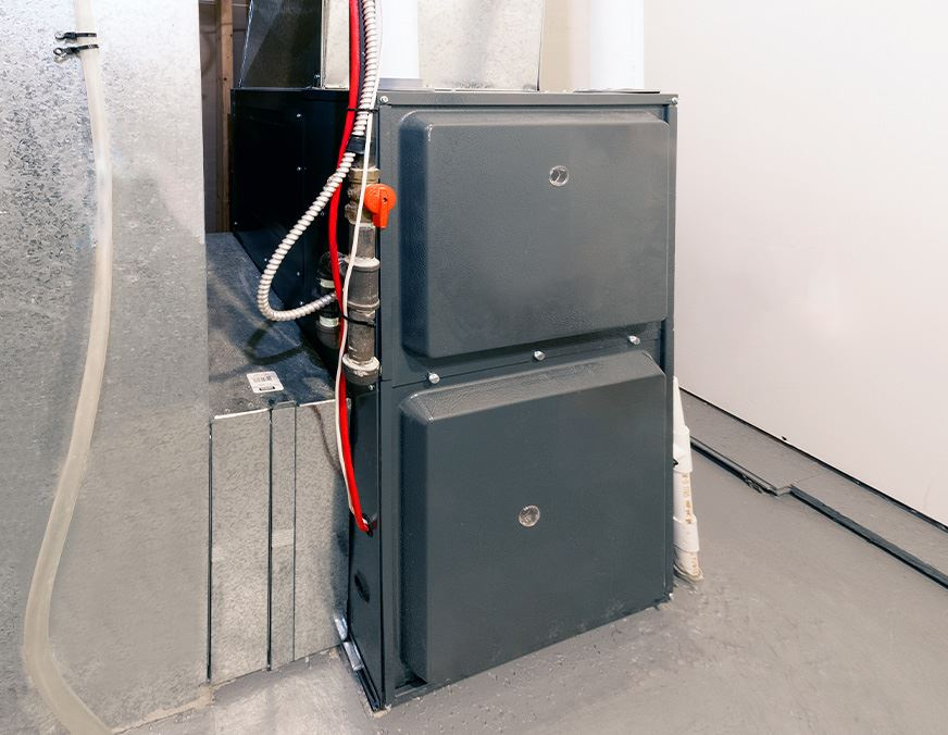 Here's a furnace with a gray exterior, alongside pipes and ducts, and placed on a concrete floor. 