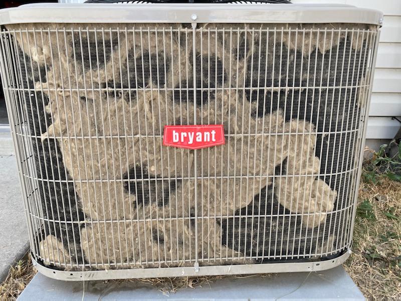 Bryant AC unit with a metal grate covered in debris. 