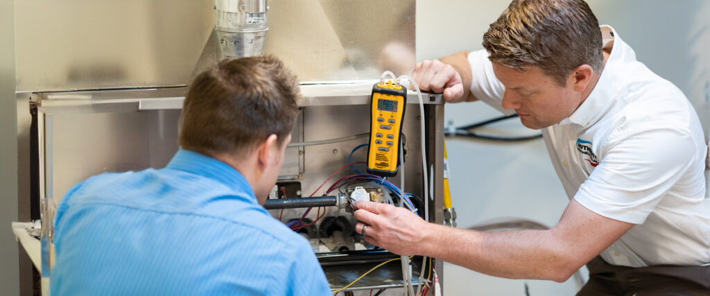 Two technicians are working on a furnace
